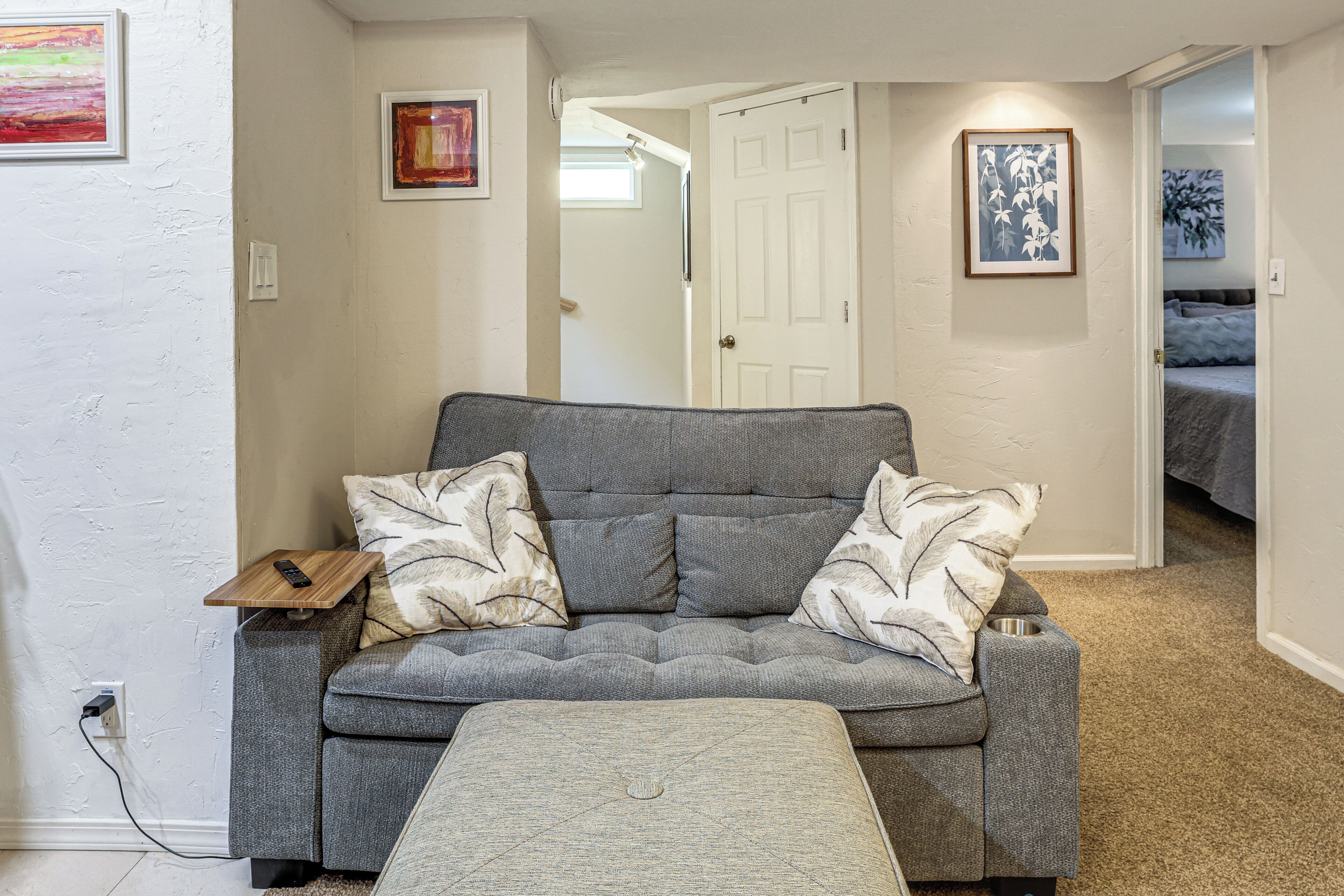 A grey sofa with patterned cushions, a small wooden side table, and a grey ottoman.