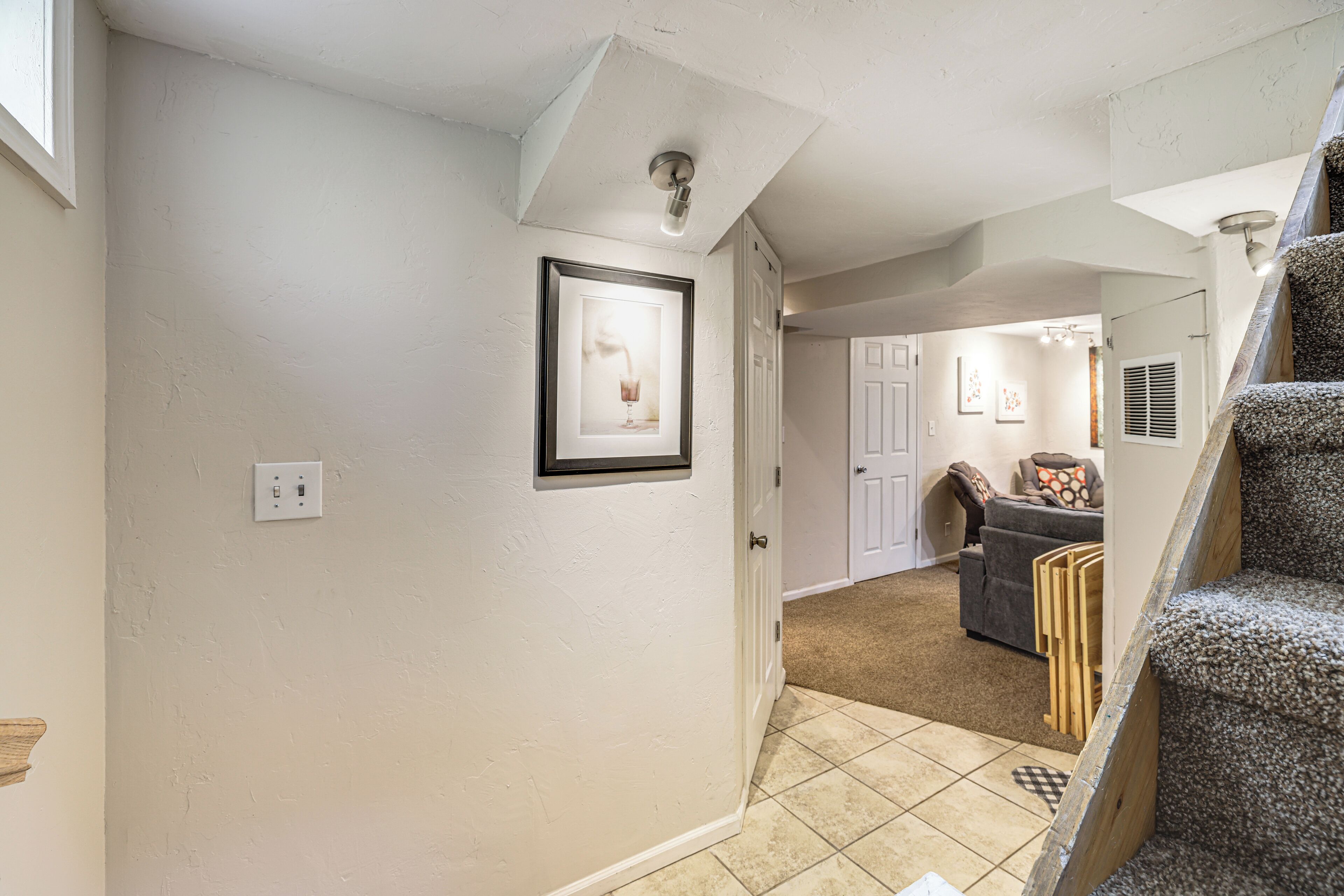 A hallway with a framed picture on the wall, a staircase, and a door leading to a living area.