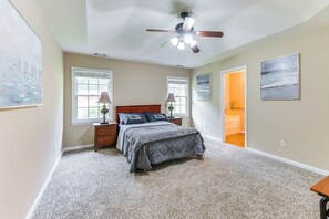 Ein Schlafzimmer mit Bett, Nachttischen, Deckenventilator und Blick ins Badezimmer.