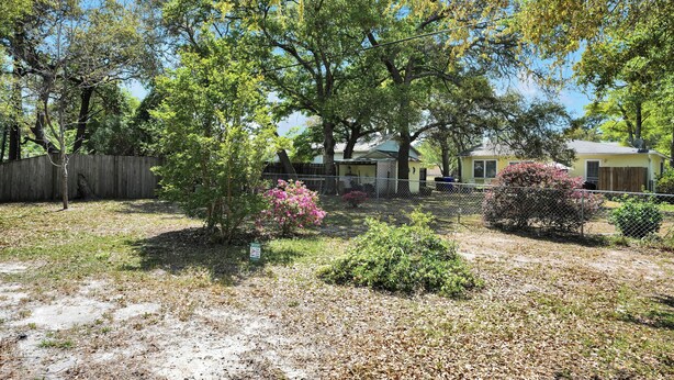 A fenced yard with trees, a small house, and a bush. - Near Eats, Shops, Golf & Beach: Oak Island Suite! (Oak Island)