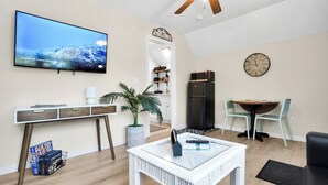 A modern living room with a flat-screen TV, a dining area with a table and chairs, a kitchen with a refrigerator, and a ceiling fan. - Near Eats, Shops, Golf & Beach: Oak Island Suite! (Oak Island)