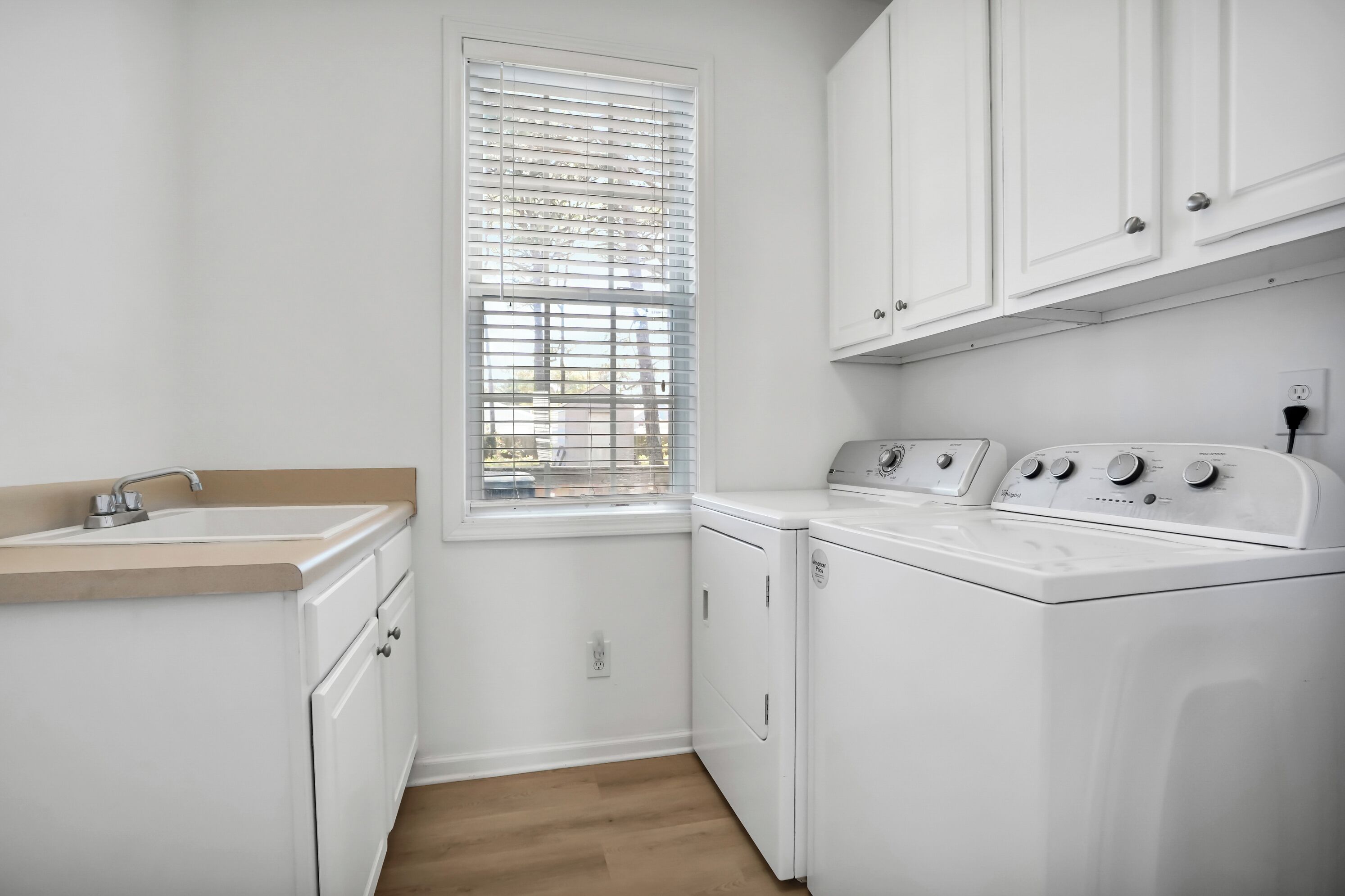 A laundry room with a sink, washing machine, dryer, and cabinets.