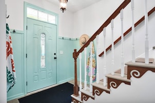 A staircase with white balusters and a wooden handrail, leading to a door with a window and a light fixture above it.