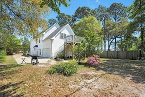 A two-story house with a covered porch, a barbecue grill, and a small patio area. - Walk to Beach Pet Friendly Beachy Summer Escape (Oak Island)