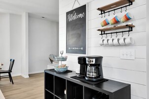 Una cocina moderna con cafetera, un pizarrón y tazas en estantes.
