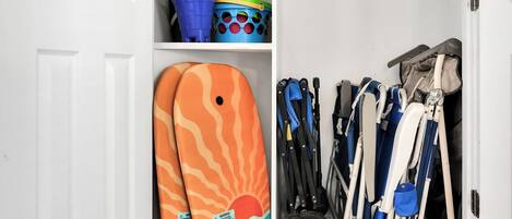 Un espacio de almacenamiento con toallas de playa coloridas, un cubo azul y verde, y varios sillones plegables.