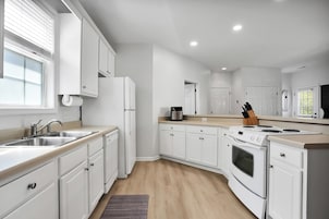 A modern kitchen with white cabinetry, a double sink, a stove, and a refrigerator.