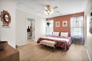 A bedroom with a bed, a ceiling fan, a window with sheer curtains, and a wall-mounted mirror.