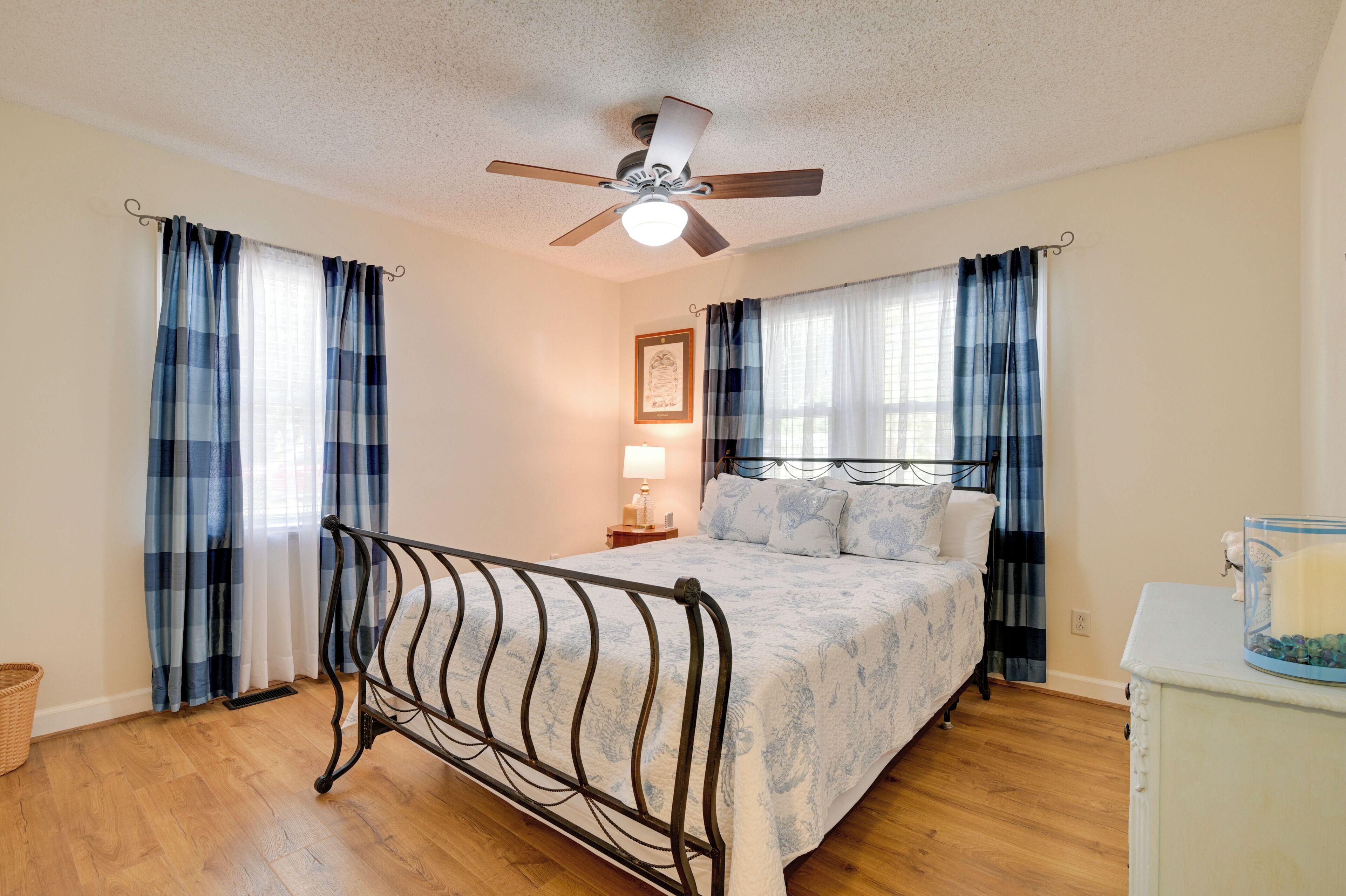 A bedroom with a bed, curtains, a ceiling fan, a bedside table, and a lamp.
