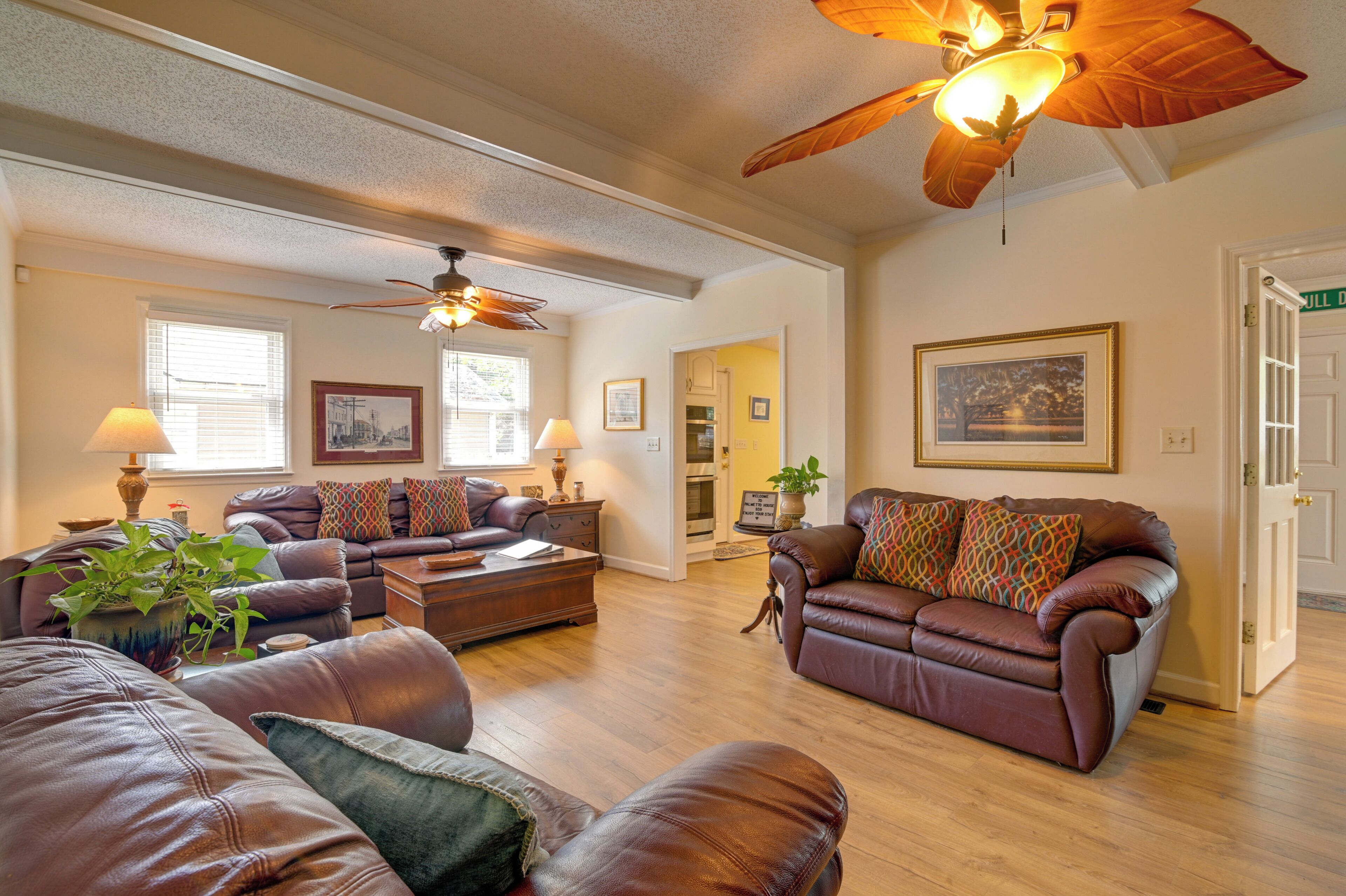 A spacious living room with leather sofas, a ceiling fan, and a dining area with a table and chairs.