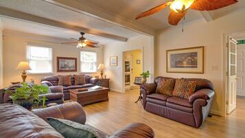 A spacious living room with leather sofas, a ceiling fan, and a dining area with a table and chairs.