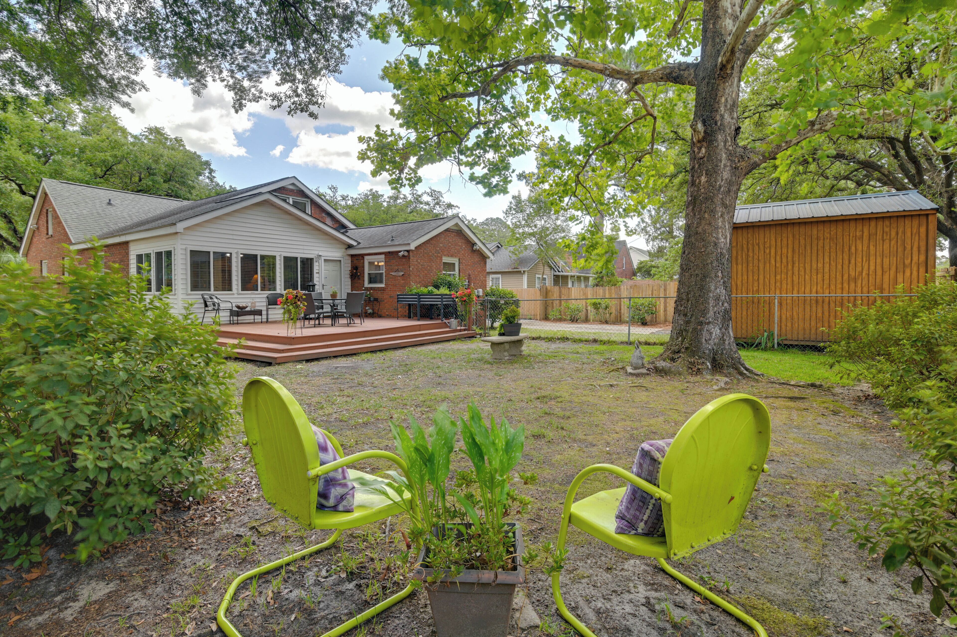 Ein Garten mit Terrasse, zwei grünen Stühlen, einem Grill und einem Holzschuppen.