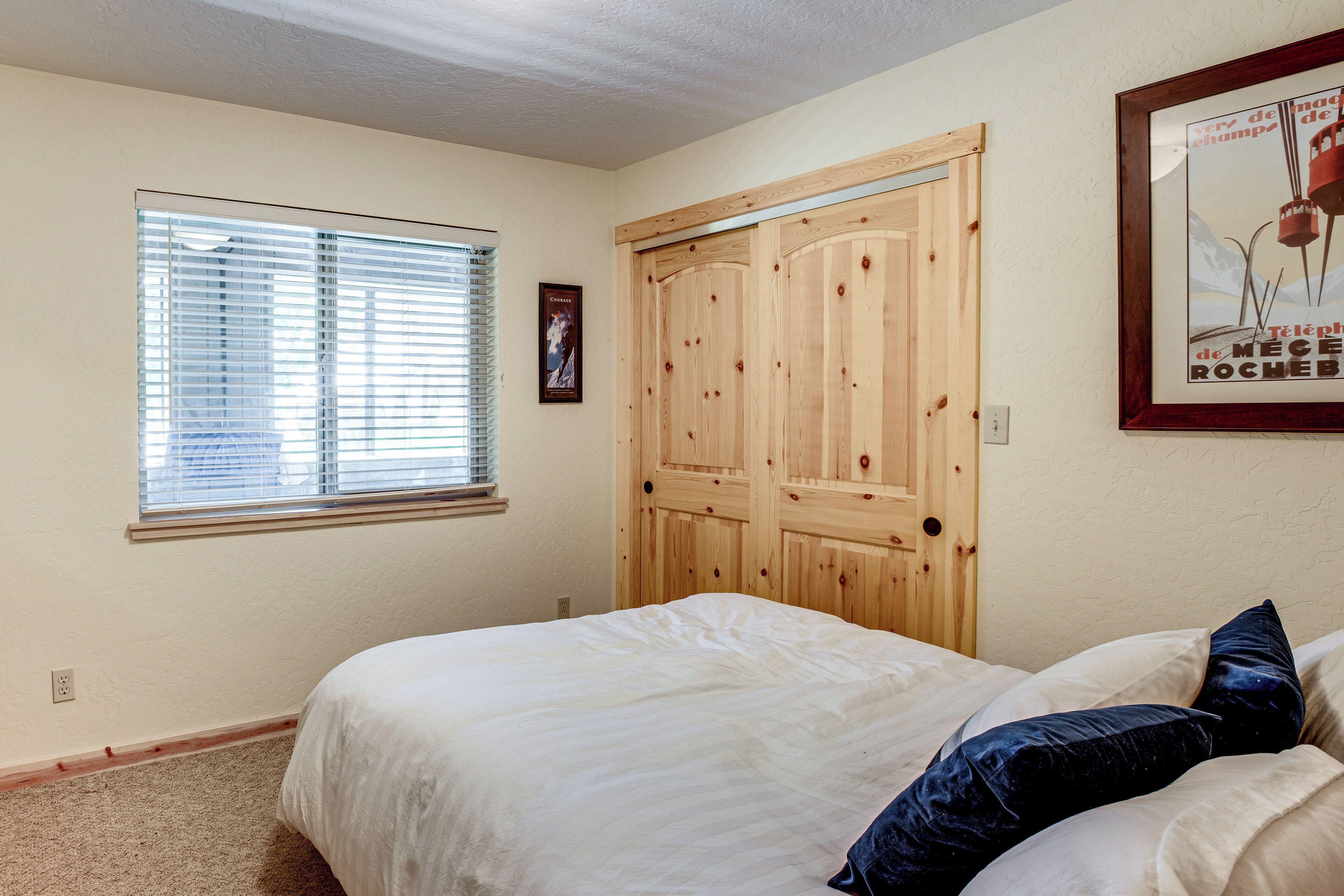 Une chambre à coucher avec un lit, une fenêtre avec des stores, une porte en bois et un tableau encadré au mur.