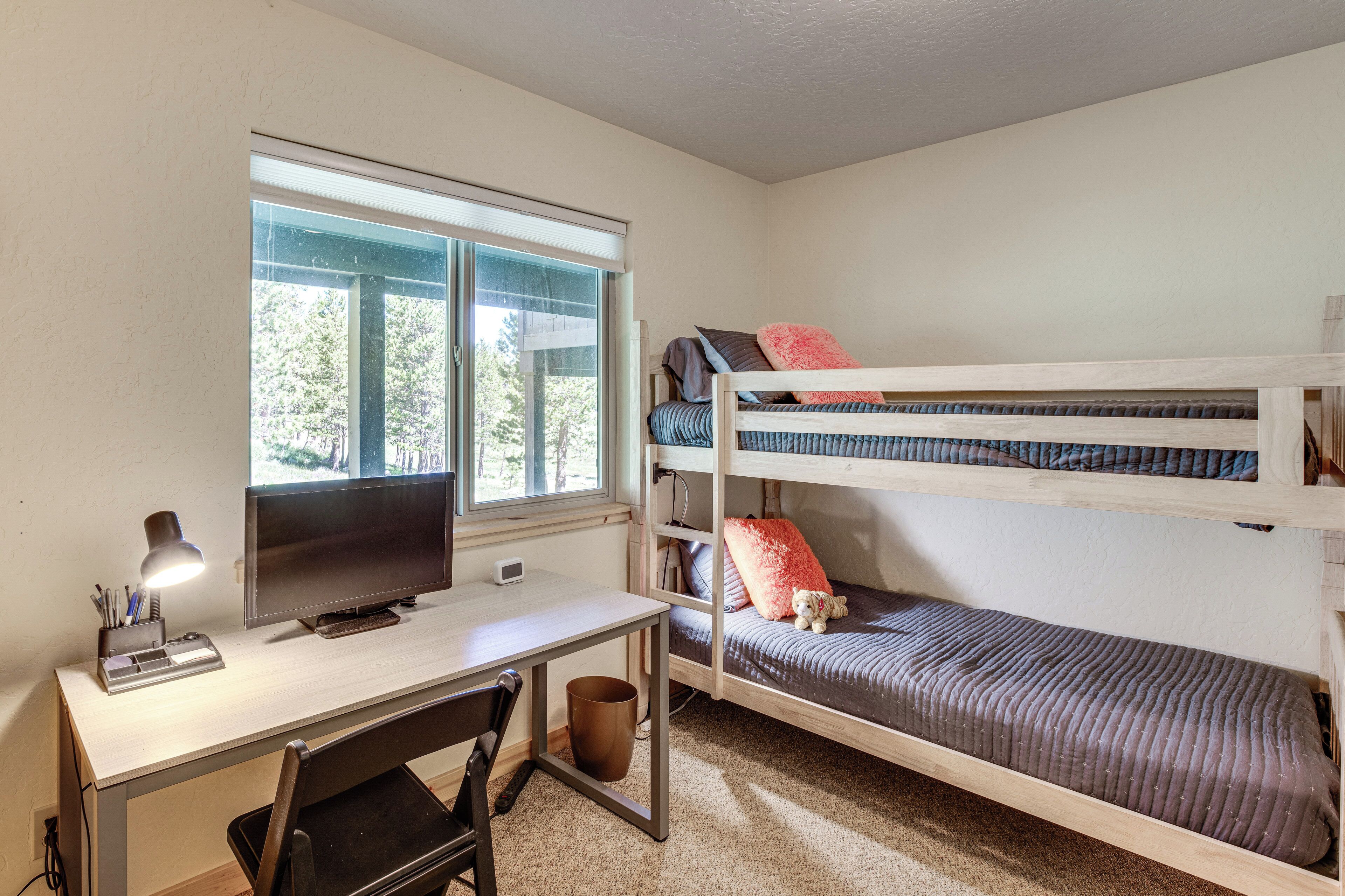 A bunk bed with a desk and a TV, a window with blinds, and a small trash can.