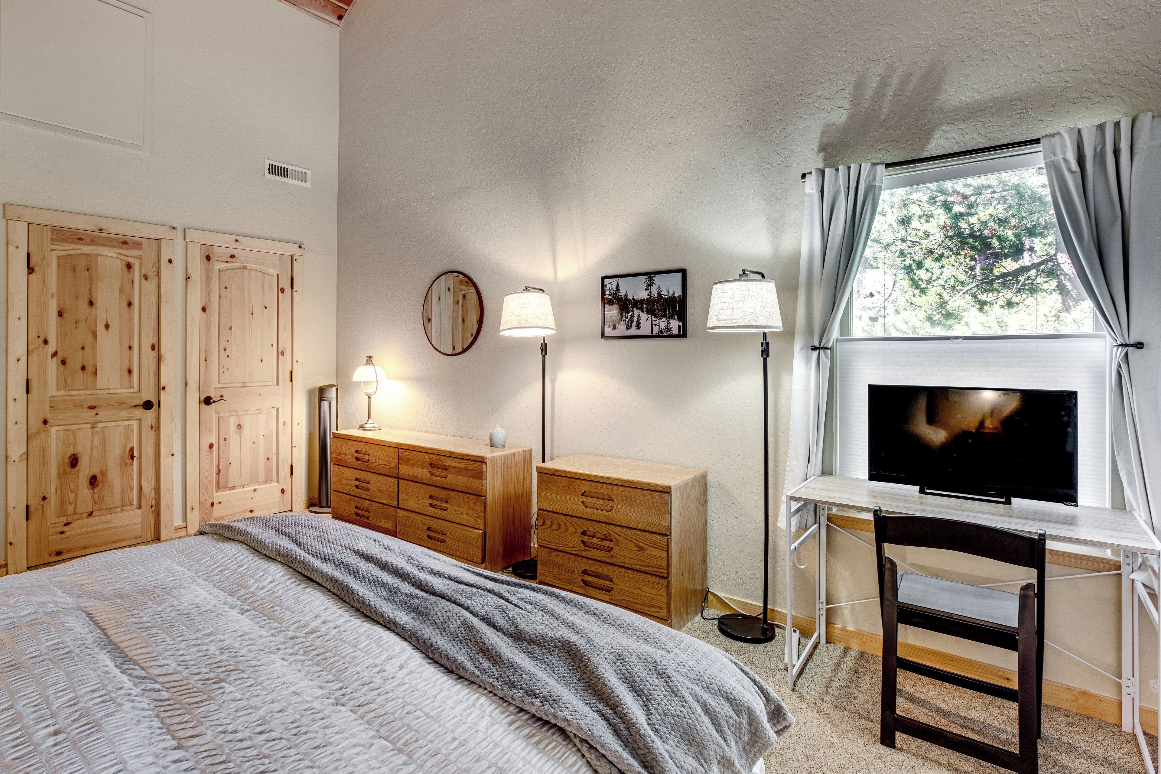 Un dormitorio con cama, armario de madera, escritorio con televisor y ventana con cortinas.