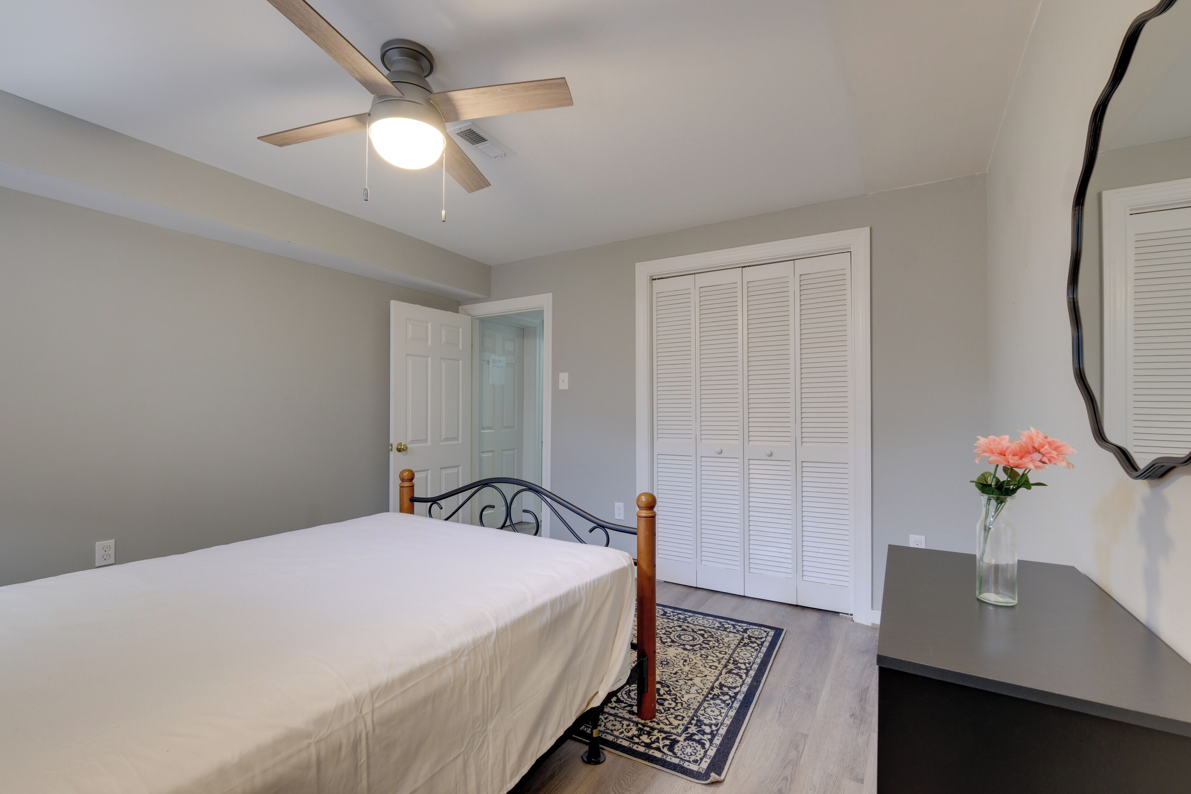 A bedroom with a bed, a ceiling fan, a door, and a mirror on the wall.