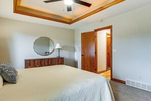 A bedroom with a bed, a wooden headboard, a ceiling fan, a mirror, and a door leading to another room.