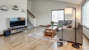 Ein modernes Wohnzimmer mit Flachbildfernseher, einer Holzunterhaltungsecke, Sofa, Couchtisch, Stehlampe und einer Treppe.