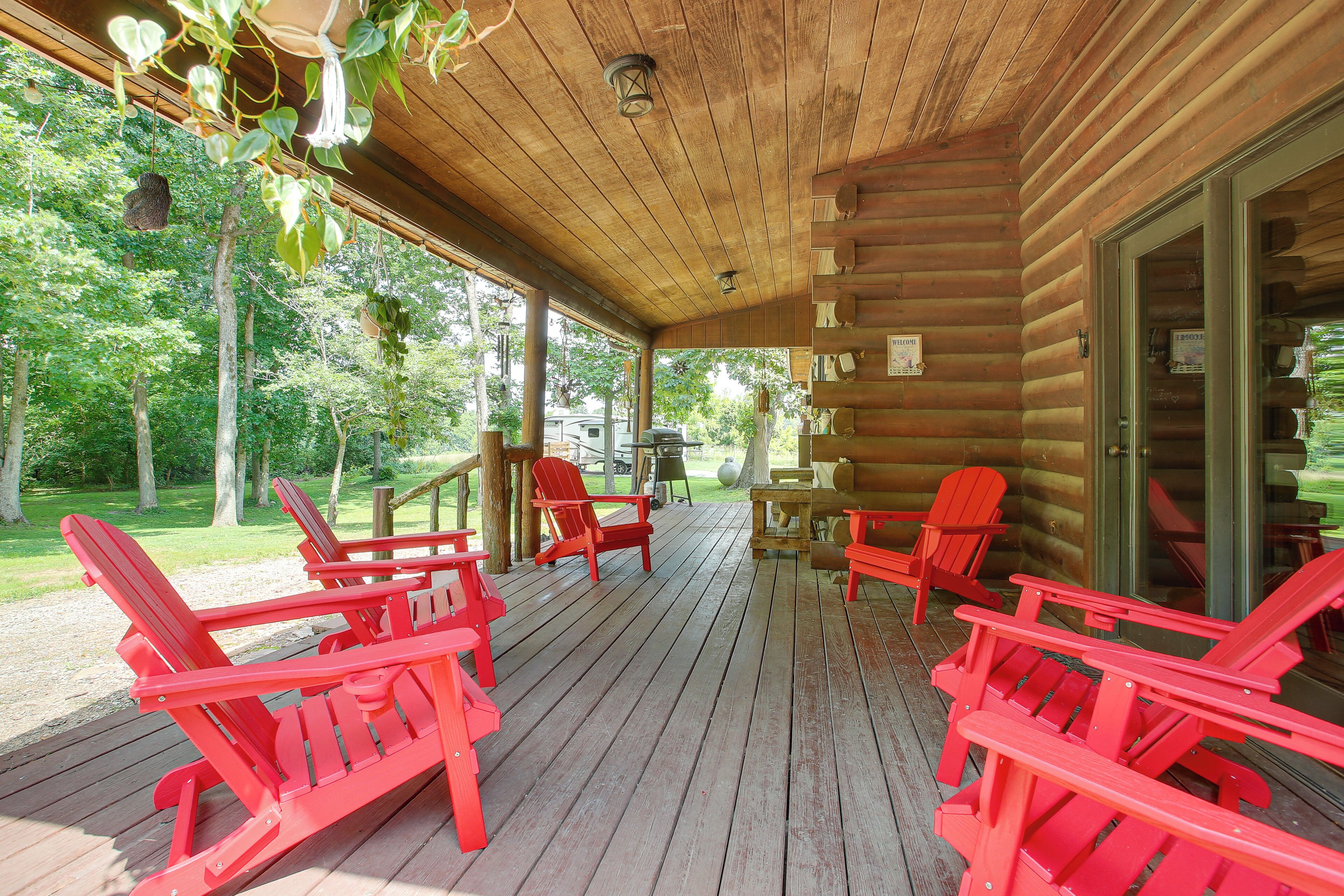 Une terrasse en bois avec des fauteuils Adirondack rouges, une table et une porte vitrée donnant sur un chalet.