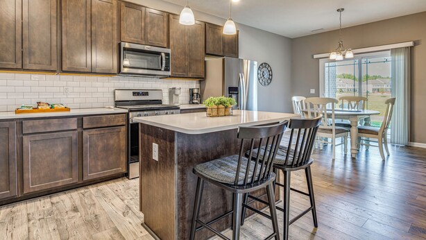 A modern kitchen with dark wooden cabinets, a stainless steel refrigerator, and a central island with bar stools. - Relax Poolside! Retreat 11 Mi to Eagle Creek Park (Whitestown)