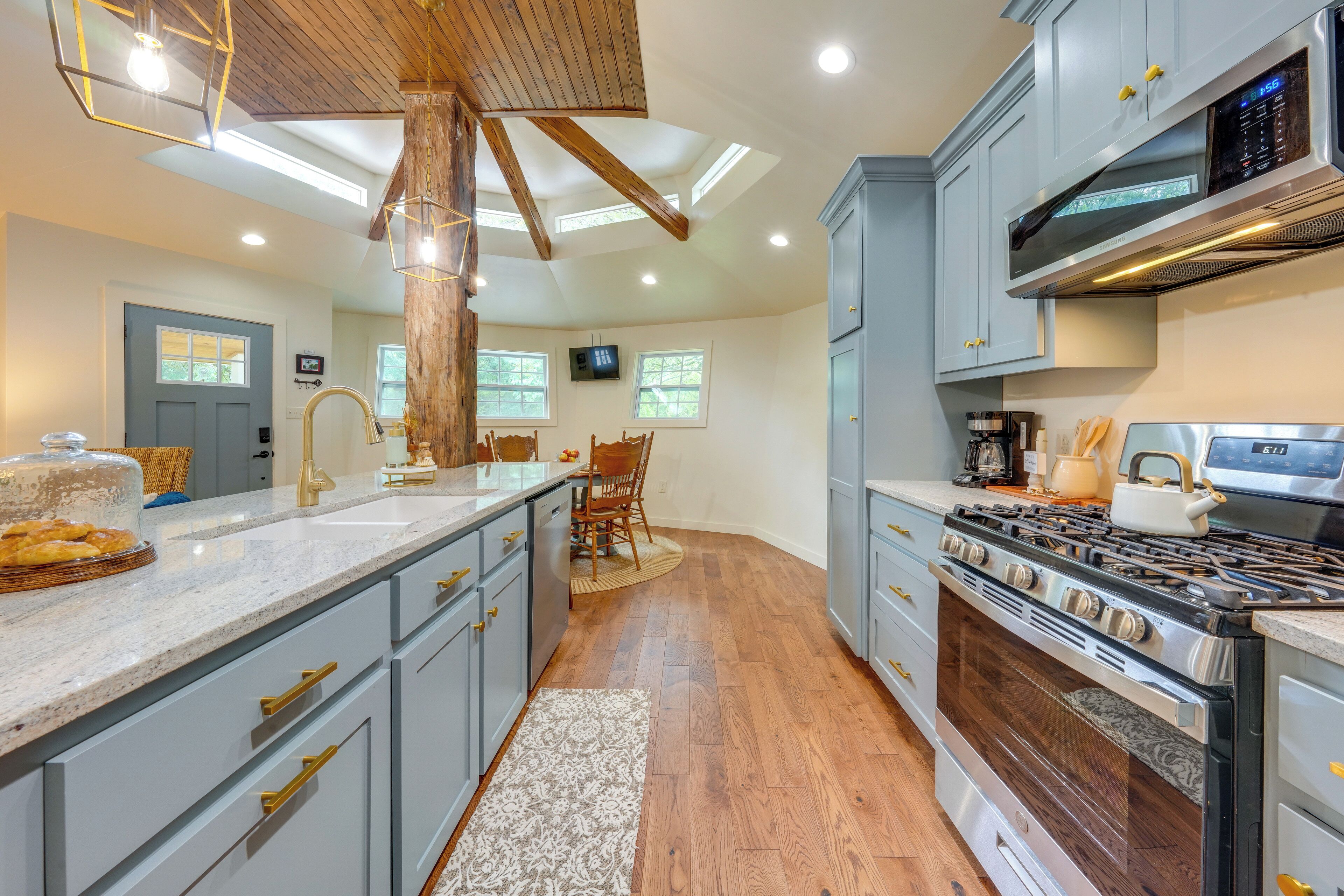 A kitchen with a large island, wooden ceiling beams, a built-in oven, and a microwave.
