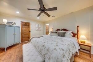 Quarto com cama, ventoinha no teto, guarda-roupa de madeira e mesa de cabeceira com abajur.