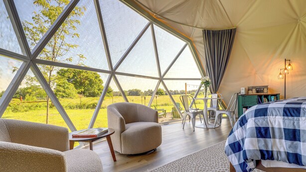 A tent with a geometric window design, a bed with a checkered bedspread, a chair, and a small table with a book.