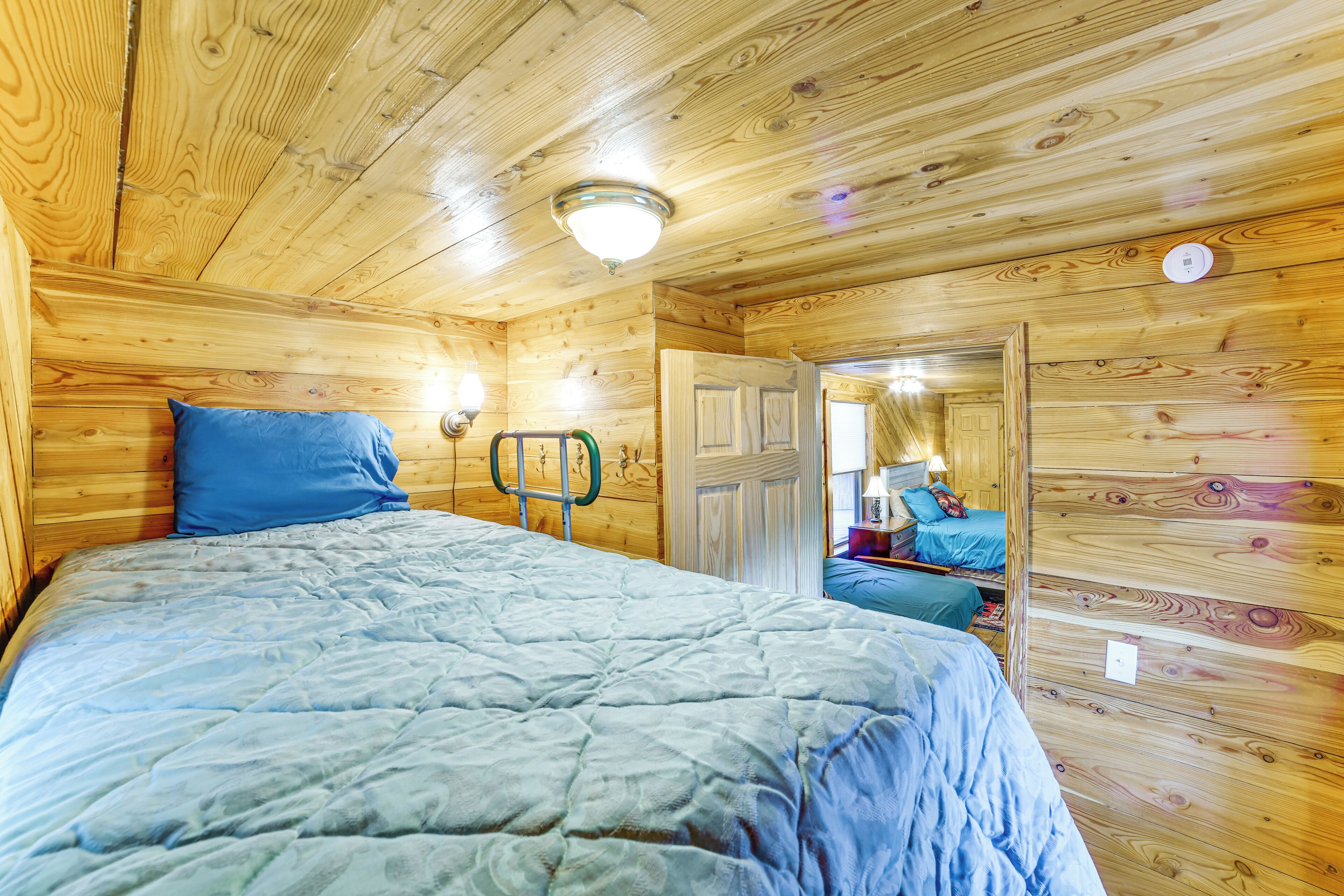 A wooden-paneled room with a bed, a door, and a mirror.