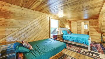Un dormitorio acogedor en el ático con paredes de madera y techo inclinado, con dos camas con ropa de cama azul a juego y una alfombra estampada.