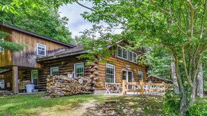 A log cabin with a porch, a stack of firewood, and a dining table.