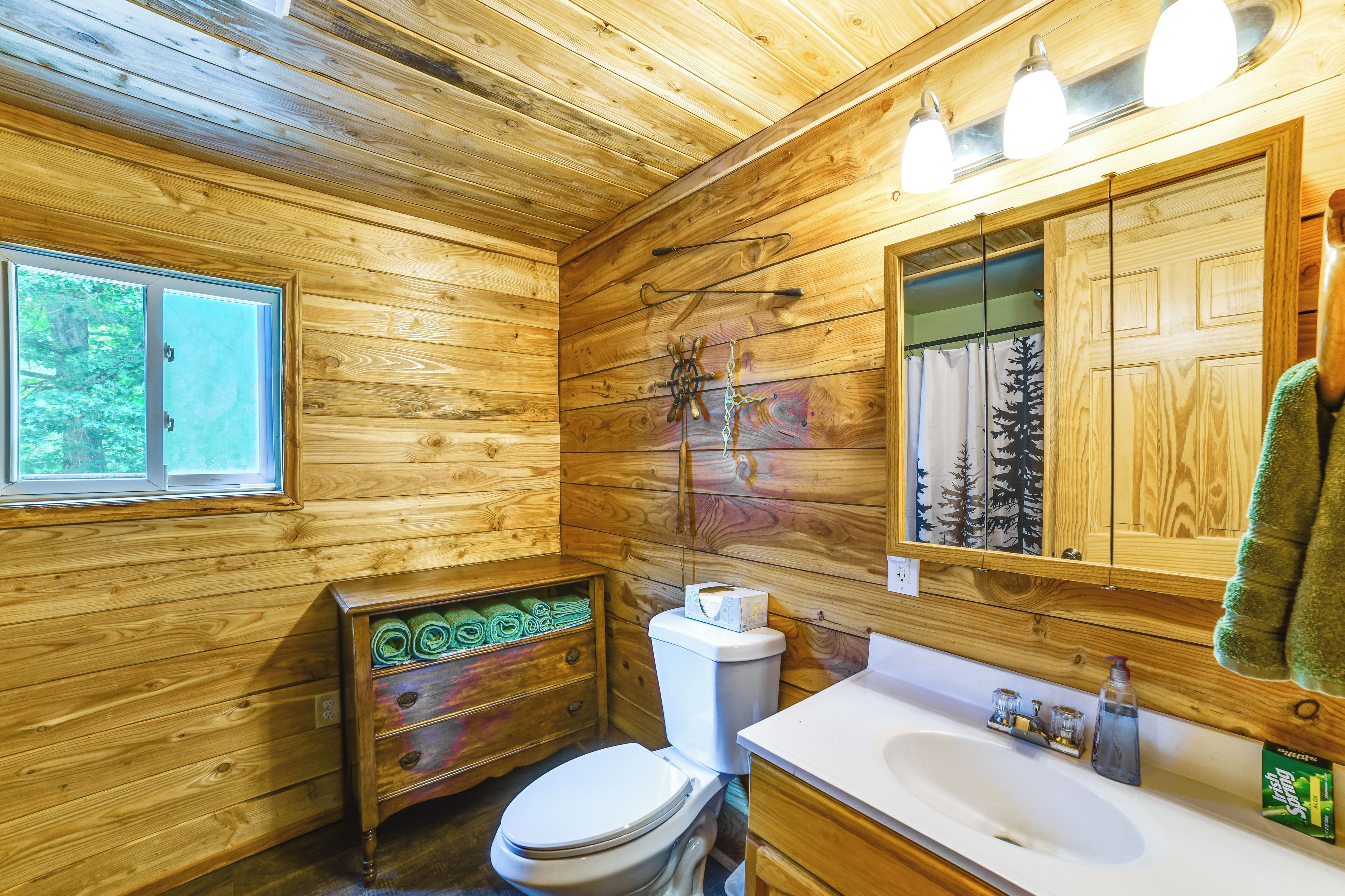 A wooden cabin bathroom with a toilet, sink, and window.
