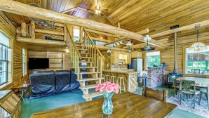A wooden interior with a staircase, a sofa, a dining table, and a vase of flowers.