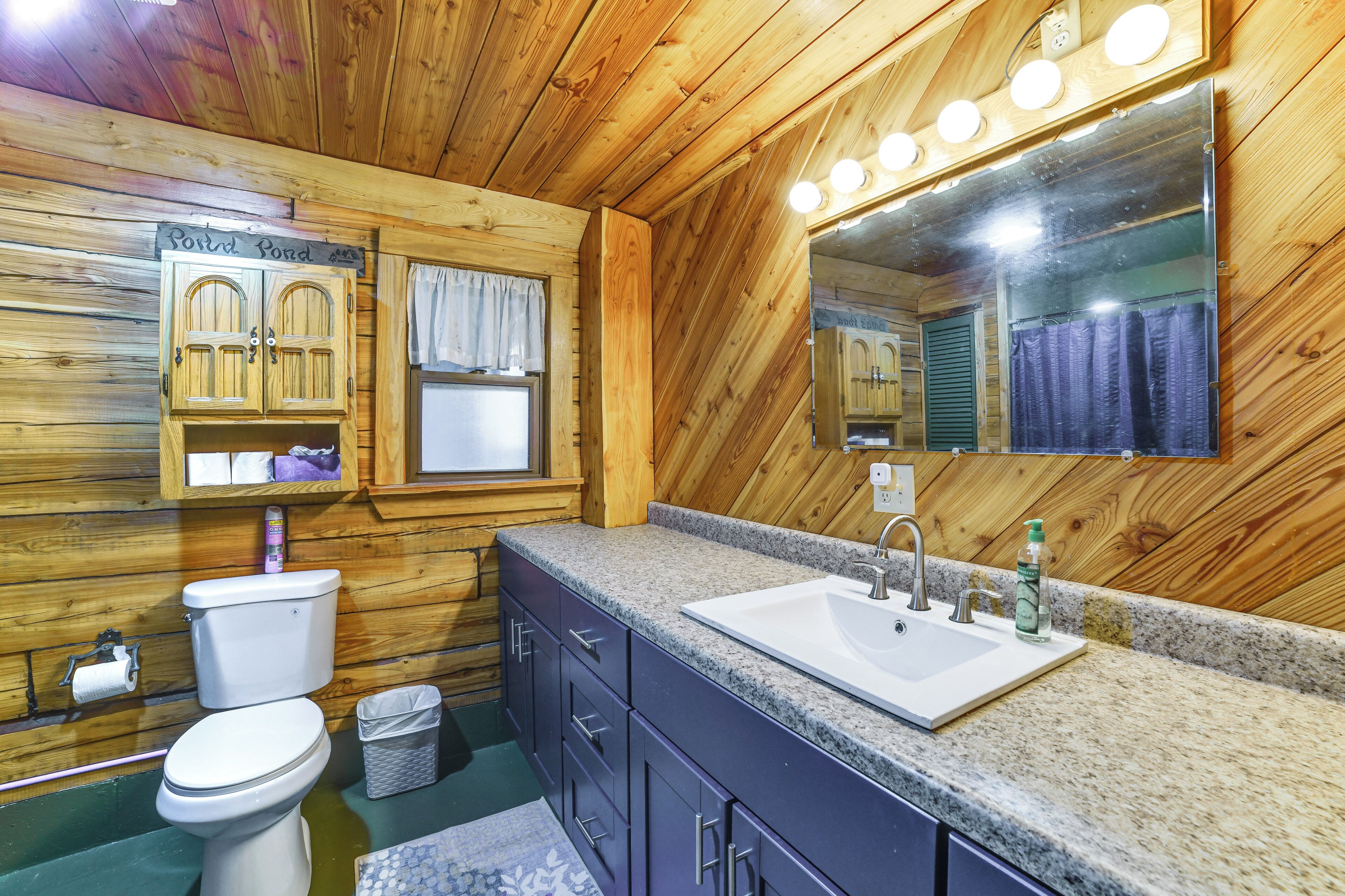 A wooden cabin bathroom with a toilet, sink, vanity, and mirror.