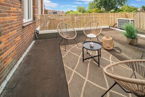 An outdoor patio with two wicker chairs, a small round table, and a potted plant.