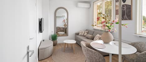 A modern living room with a sofa, chairs, a coffee table, a TV, and a large window with blinds.