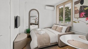 Une chambre moderne avec un lit, des tables de chevet, un miroir, une fenêtre avec des stores et un climatiseur fixé au mur.