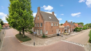 Une rue résidentielle bordée de maisons en briques, avec des trottoirs pavés et un grand arbre.
