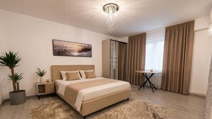 Moderni hotellihuone, jossa on suuri sänky, yöpöytä, pieni pöytä, ruukkukasvi, taulu ja näkymä ulos.