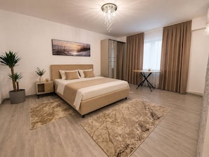 Ein modernes Hotelzimmer mit einem großen Bett, einem Nachttisch, einem kleinen Tisch, einer Zimmerpflanze, einem Gemälde und Blick ins Freie.