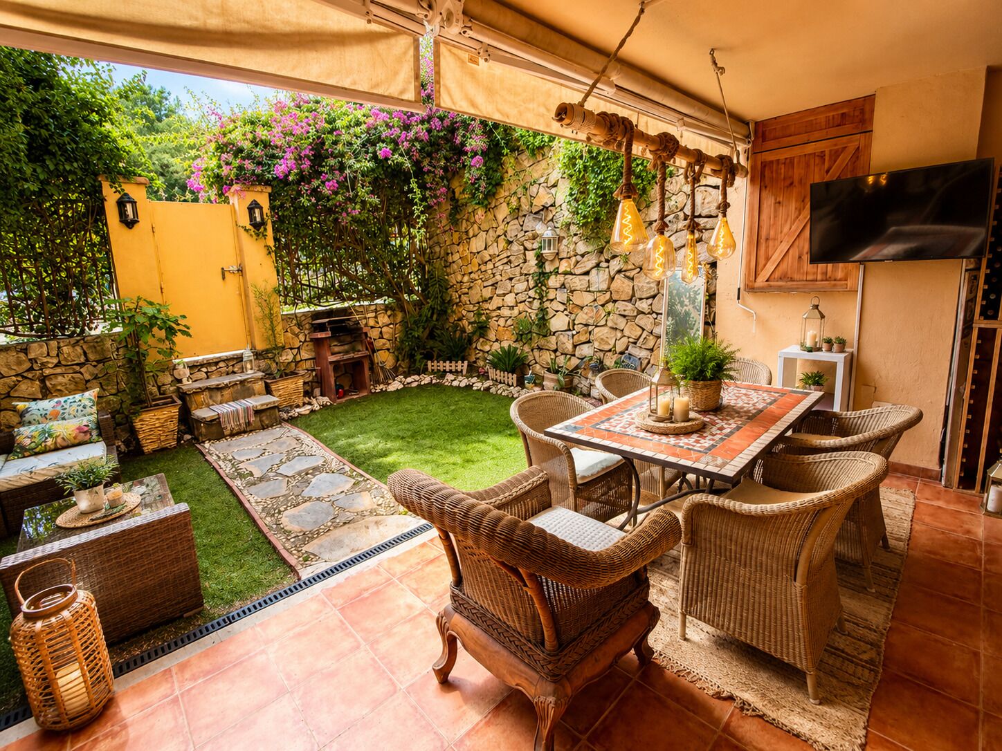 Une terrasse avec un mur en pierre, une porte jaune et un téléviseur fixé au mur.