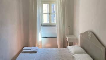 A bedroom with a bed, a nightstand, a window with curtains, and a view of the outside.