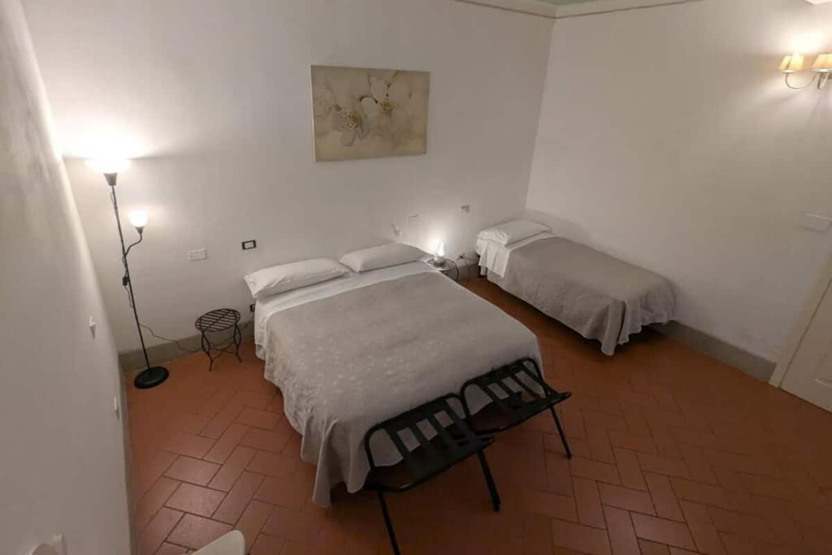 A room with two beds, a standing lamp, and a wall-mounted light fixture.