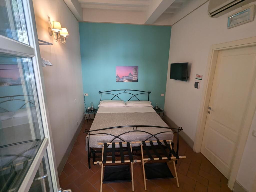 Quarto com cama, janela, televisão na parede e porta.