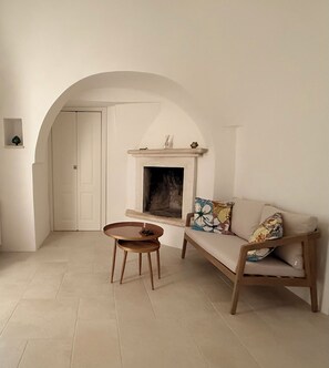A minimalist living room with a sofa, a round wooden table, and a fireplace. - Musorosso Trulli (Locorotondo)