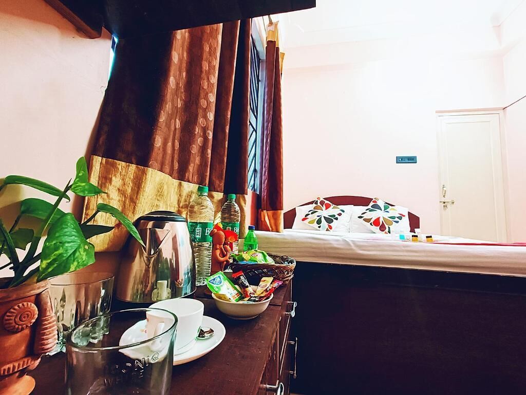 Quarto com cama, mesa com um recipiente de lanches, chaleira, xícara e planta em vaso.