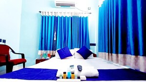 Une chambre d’hôtel avec un lit, des rideaux bleus, une chaise rouge, une table de chevet avec des articles de toilette et un appareil de climatisation.