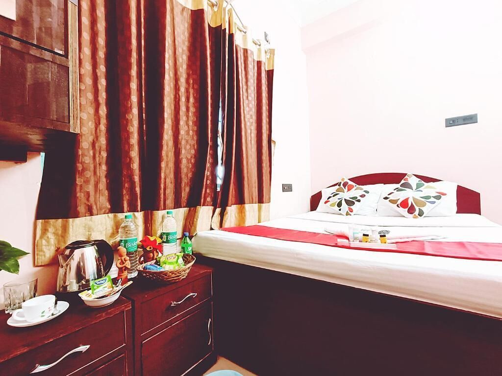 Quarto de hotel com uma cama, cómoda de madeira, espelho e janela com cortinas.
