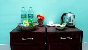 Une commode en bois avec deux tiroirs, un panier de collations, deux bouteilles de Sprite, un petit vase avec des fleurs, une théière, une tasse et un verre.