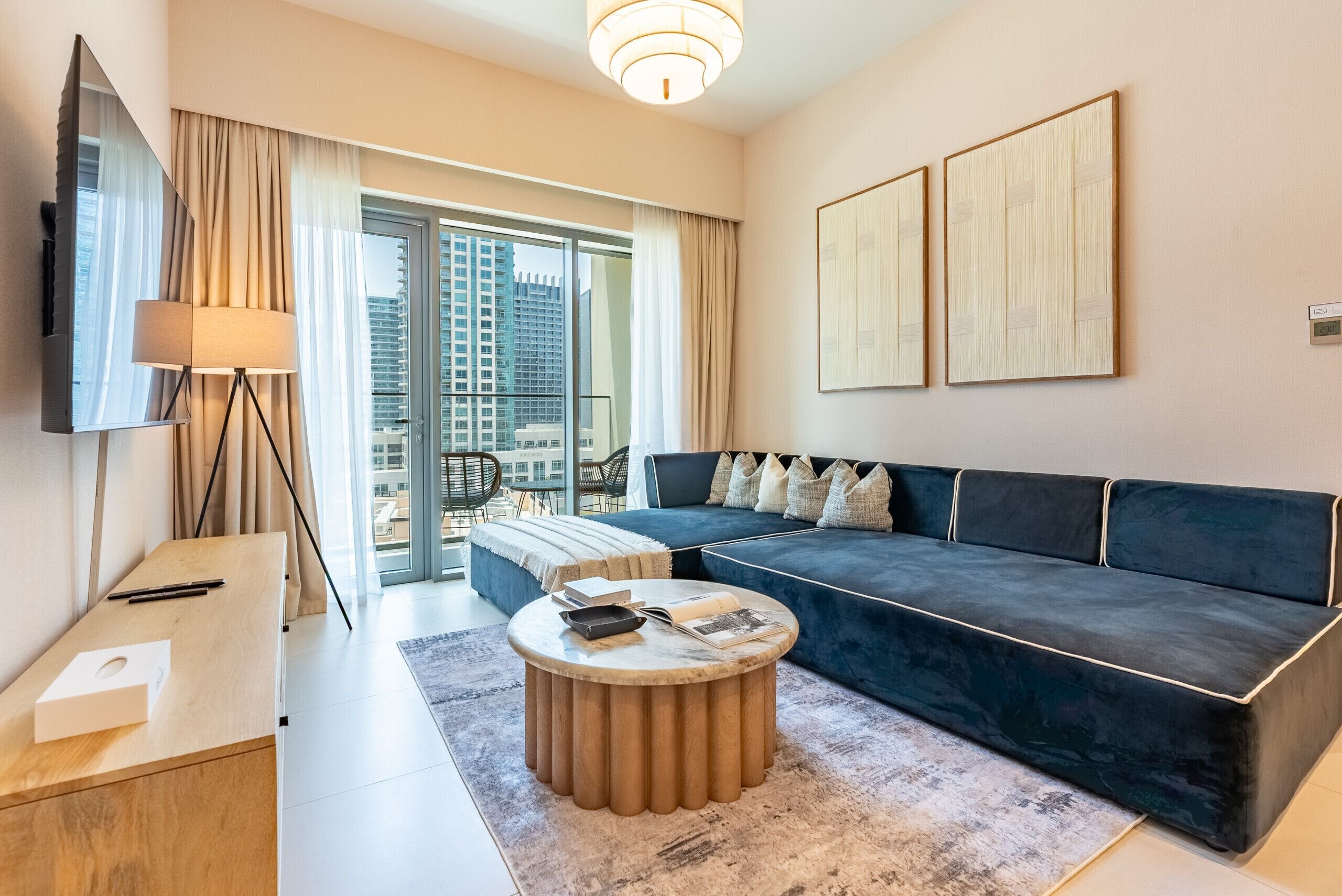 Une chambre d’hôtel moderne avec un grand canapé, une table basse ronde, un bureau avec une lampe et un téléviseur.
