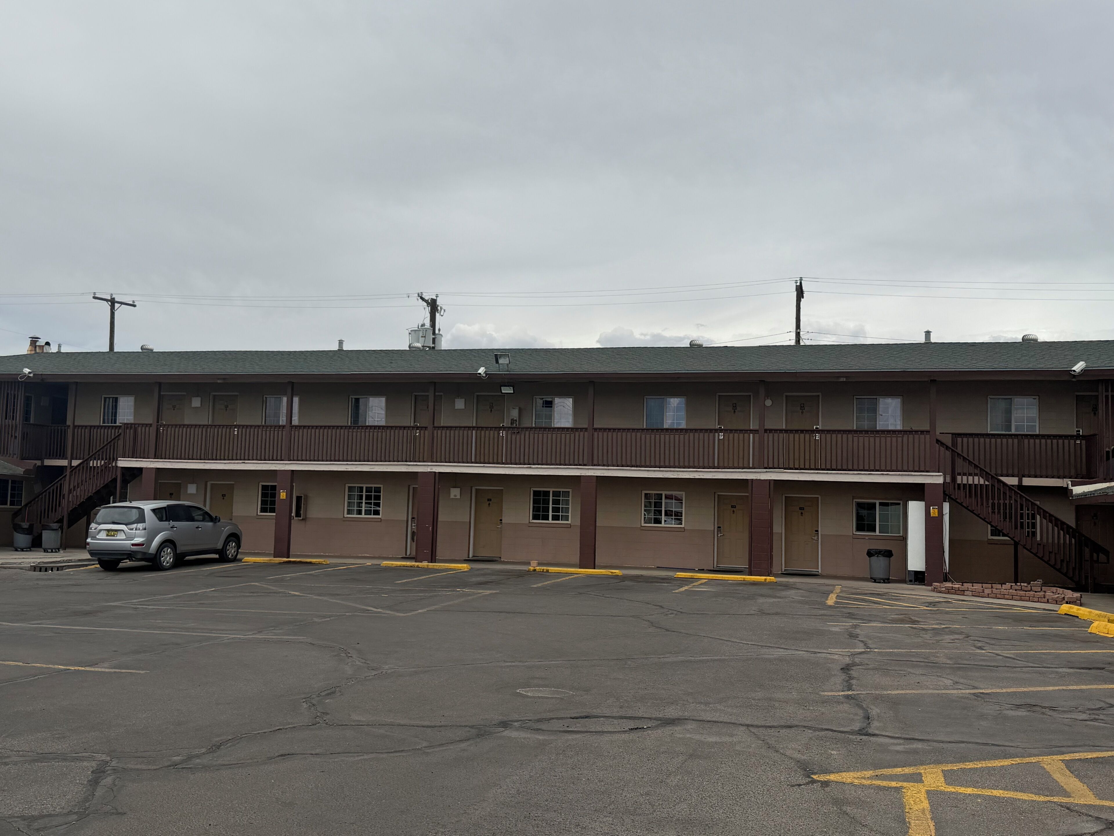A motel with a parking lot, multiple rooms, and a staircase leading to the upper floor.
